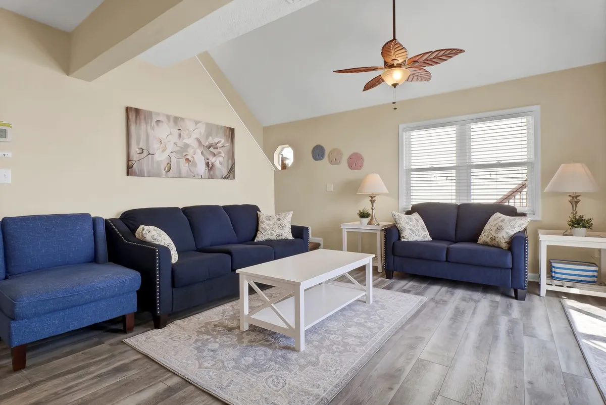 A cozy living room with a comfortable sofa set, coffee table, wall art, and a ceiling fan, arranged in a way that encourages relaxation, socializing, and family time. The decor is warm and inviting, enhancing the sense of home within the duplex.