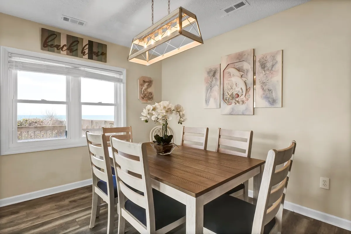 A warm, welcoming dining area with a large table, chandelier, wall art, and a sunlit window. The setup encourages shared meals, celebrations, and conversations, perfectly sized for family or group gatherings.