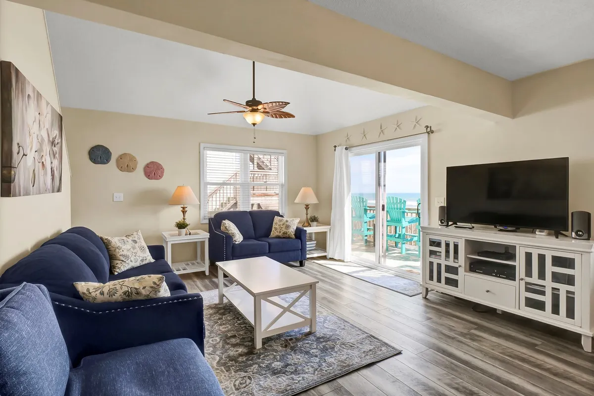 A cozy living room with plush sofas, a coffee table, a large television, and sliding doors to the balcony. The setup is perfect for relaxing with family, watching movies, playing games, or simply enjoying the view outdoors.